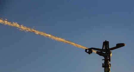 Sun shines in the stream of a Nelson Irrigation Part-Circle Impact Sprinkler