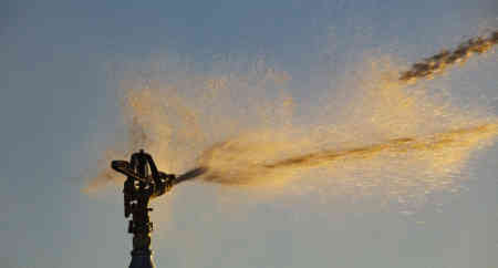 Sun shines in the stream of a Nelson Irrigation Part-Circle Impact Sprinkler